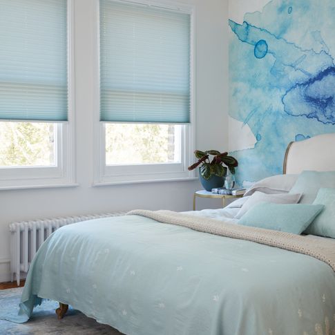 Light blue Pleated blinds dressed on windows of white painted bedroom. There is matching light blue duvet and pillows on the bed.