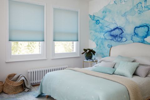 Light blue Pleated blinds dressed on windows of white painted bedroom with feature wall having abstract blue design.