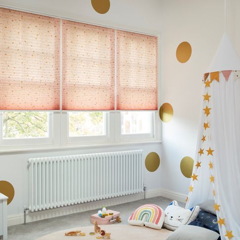 Light pink blind with gold dots printed Pleated blinds dressed on windows of kids' bedroom.
