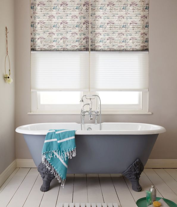 Transition blinds in sheer white and tree patterns in blue and plum at window, above a blue rolltop bath.