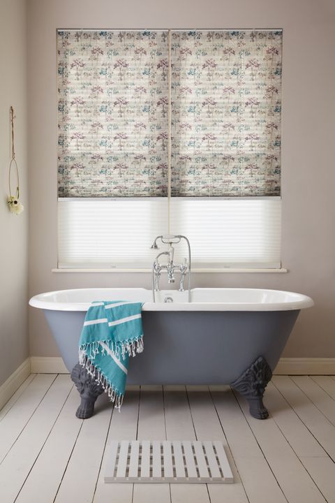 Transition blinds in sheer white and neutral with tree patterns in blue and plum at window, above a blue rolltop bath with a blue striped towel.