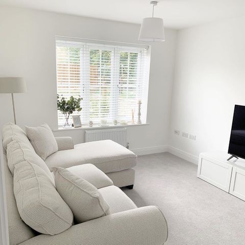 White wooden blinds hanging on the windows of white painted living room.  Cream sofa has been placed in the room.
