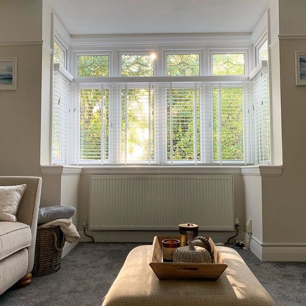 Living room with cream walls and sofas featuring bay window with white wooden veneitan blinds 