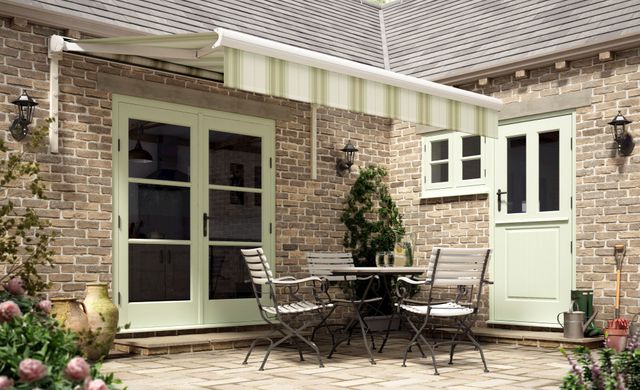 Beige and green striped awnings installed on a wall with patio doors. Garden table and chairs are placed under awnings