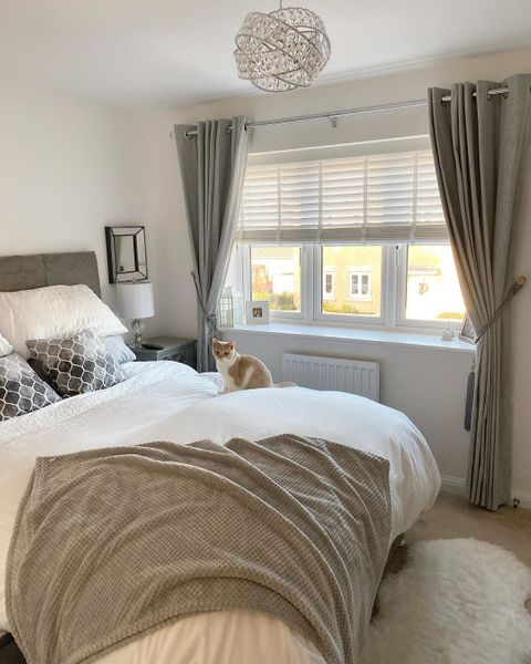 White wooden blinds dressed under grey curtains on the windoes of bed room