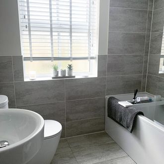 Wooden blinds dressed on window of bathroom , walls decorated with grey tiles