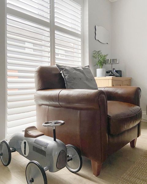 White shutters behind brown leather armchair with grey toy car