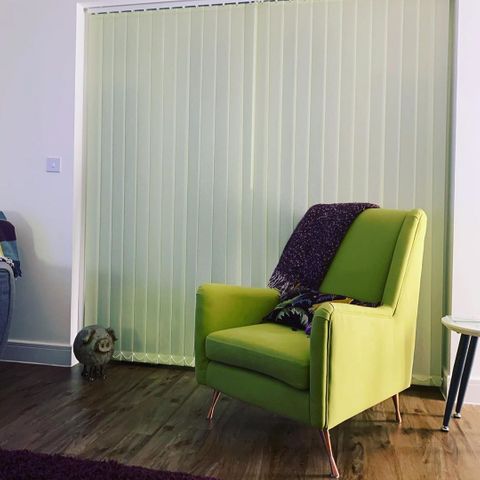Light green vertical blinds dressed on door of living room. Green sofa has been placed in front of the blinds.