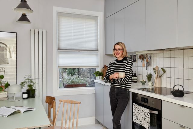 Someone standing in a white kitchen with white transition blinds fitted to rectangular window