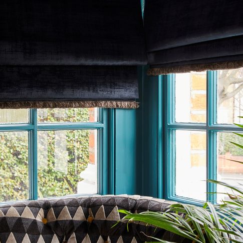Black coloured roman blinds fitted to teal coloured windows in a room 