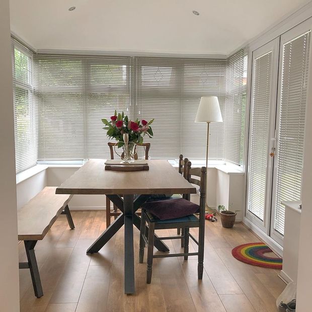 Grey perfect fit blinds with white lamp and large wooden table with bunch of flowers