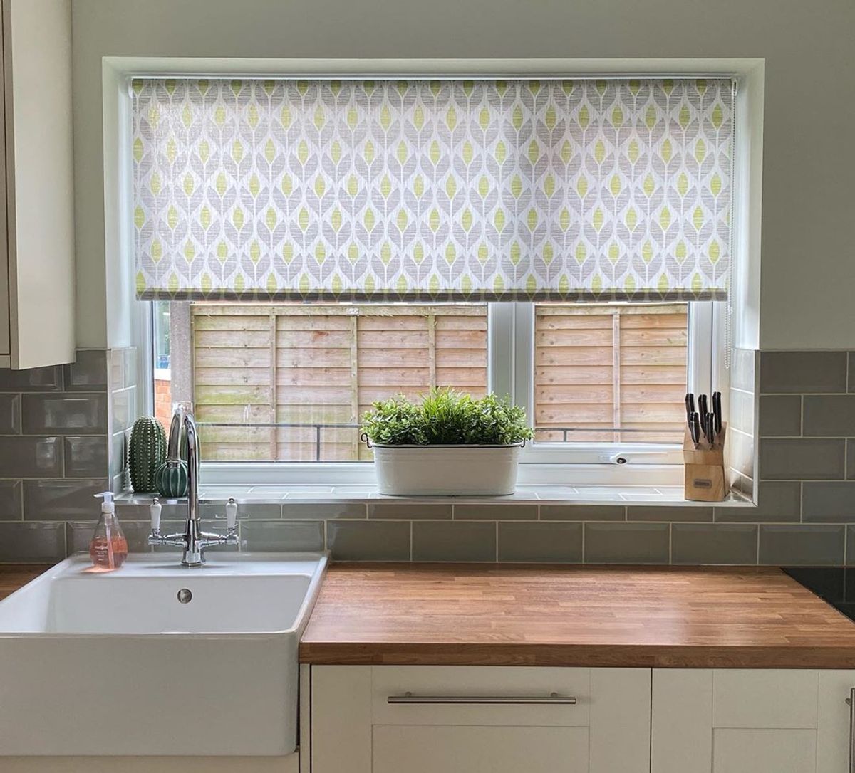 Petula Ochre Roller blind in kitchen behind wooden counter and white sink with green tiles and ceramic cacti