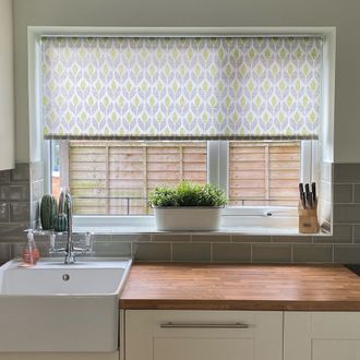 Petula Ochre Roller blind in kitchen behind wooden counter and white sink with green tiles and ceramic cacti