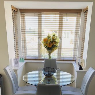Wooden Venetian blinds in a square bay window with bouquet of flowers, 'new home' cards and glass dining table