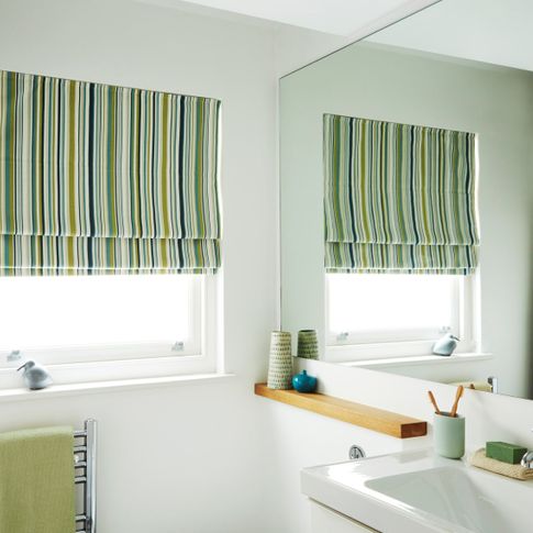 City Spruce roman blind decorated in different stripes of green is fitted to a tall window in a bathroom with a large window and painted white