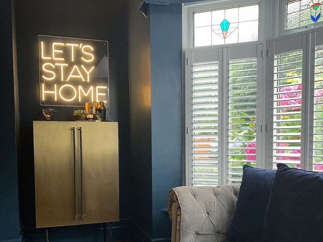 living room with dark blue walls and white shutters with a let's stay home neon sign
