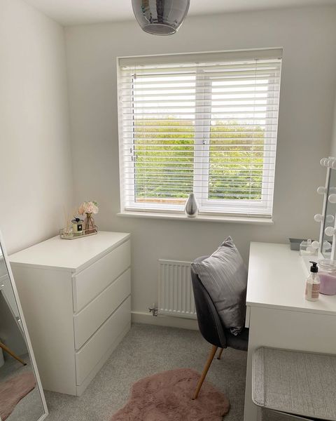 white blinds in beauty room with white drawers, grey chair and pink rug