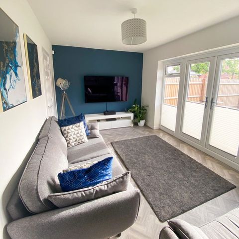 white pleated blinds pulling half way up from the bottom of the patio doors allowing light into the room with a navy wall, TV and grey sofa with blue cushions