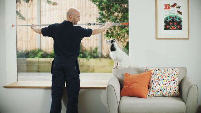 Advisor measuring window with black and white dog on sofa arm next to him