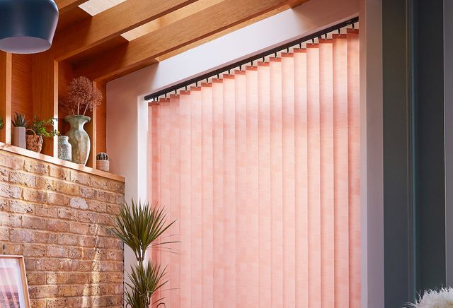 peach coloured vertical blinds fitted on a wide window in a living room with exposed brick work and wood slats