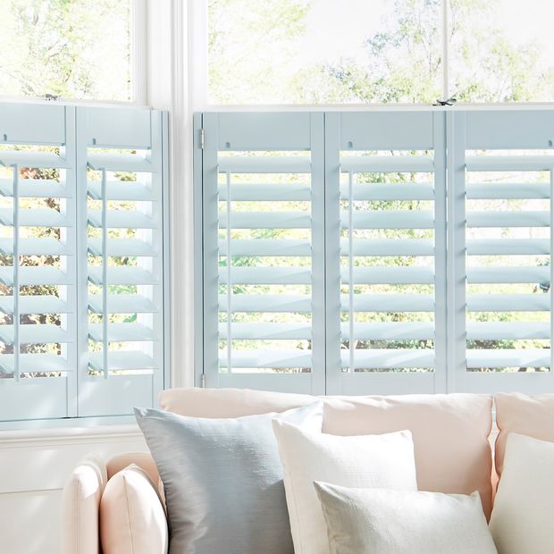 duck egg blue cafe shutters are fitted to windows in a licing decorated in white with a sofa in front