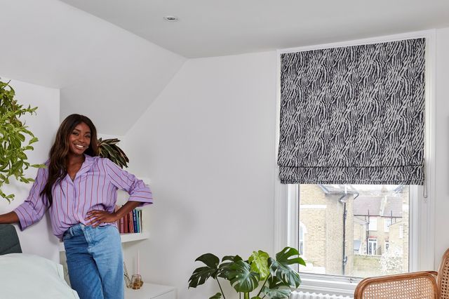 AJ Odudu in a white decorated bedroom with a grey and white patterned roman blind fitted to a rectangular window