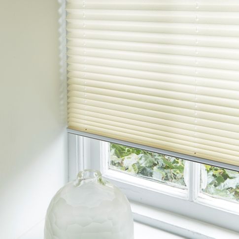A cream coloured pleated blind fitted to a rectangular window on a white window sill