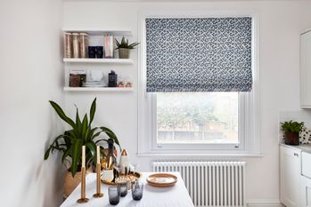 funky blue and white Roman blind behind dining table with candles and plants