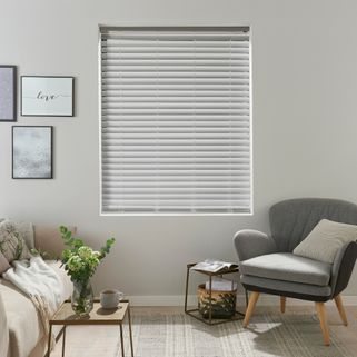 pale grey wooden Venetian blind with frames on the wall and grey arm chair with wooden legs