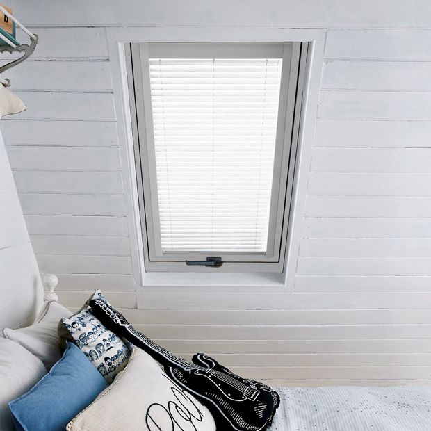 Singular loft window which are fitted with Shimmer White in a white tone. The Skylight Venetian blinds are fully-closed, blocking out sunlight into the loft with bedroom and bed.