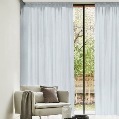 The Lyra Ivory Voile curtains in a lounge area, spanning a wide full length glass window. A gap has been left between the voiles to show the garden outside, whilst the voiles create privacy but allow light into the space.
