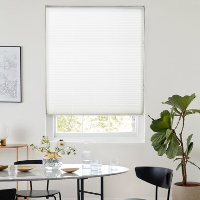 White coloured pleated blinds that are fitted to a large rectangular window in a dining that has a modern design and white walls