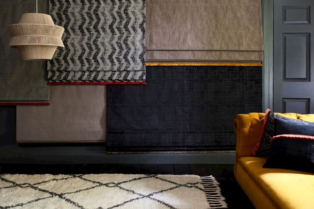 A series of fabrics from the Abigail Ahern collection hanging from a wall in a room with white and black patterned rug and yellow sofa