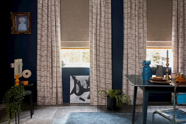 Cream coloured curtains paired with brown roman blinds both are fitted to rectangular windows in a dining room decorated in blue
