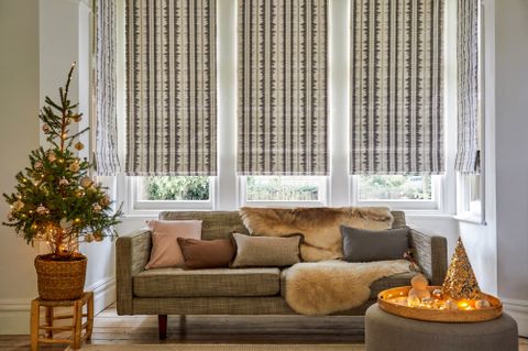 Cream and grey striped Roman blinds in a window behind a sofa and Christmas tree with gold lights and decorations