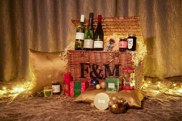 Christmas Fortnum and Mason hamper half open, filled with Christmas treats and fairy lights in the background