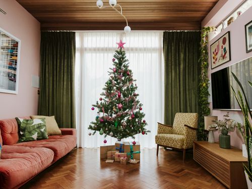 Luxe green curtains and soft white voiles layered in a large window in a room with retro decor and a Christmas tree