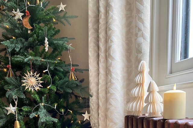 Close up of Christmas tree next to window with neutral curtains and Christmas decorations on the window sill