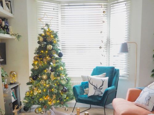 Living room with blue and peach sofas with Christmas cushions and a decorated Christmas tree infront of a window with white wood venetian blinds