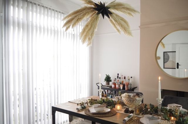Dining table decorated for Christmas with pampas grass decoration over head and white vertical blinds in the window