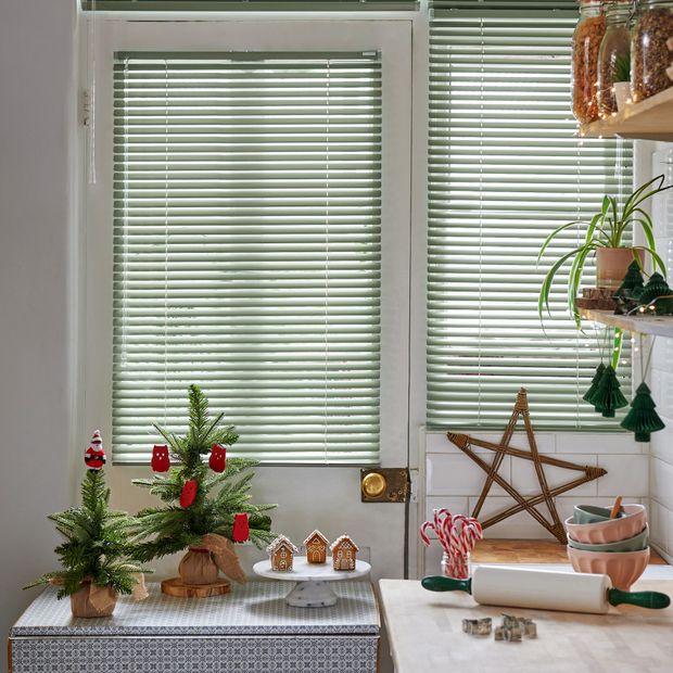 Two green venetian blinds in kitchen area with christmas trees, candy canes and gingerbread house decorations