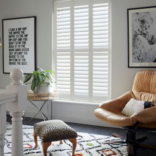 Silk white full height shutters on landing with large leather armchair, leopard print foot stool and house plant