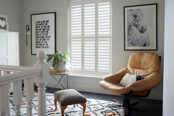 Silk white full height shutters on landing with large leather armchair, leopard print foot stool and house plant