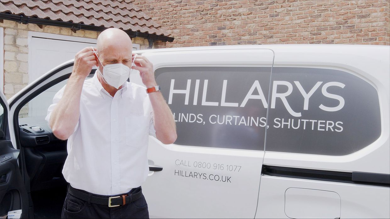 A Hillarys advisor putting on a face mask next to a van before entering a customers home