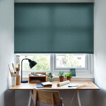 A small office space with the Battersea Peacock Roller blind freely hanging in a window above the desk. The jacquard design is set against neutrally decorated walls.