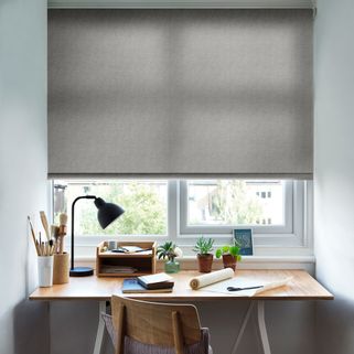 A small office space with the Harrow Charcoal Roller blind freely hanging in a window above the desk. The printed design is set against neutrally decorated walls.