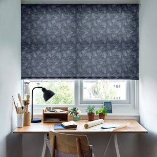 The Palm Springs Imperial Roller blind hanging above a wooden desk in a home office. The jacquard imperial blind covers three quarters of the large window.