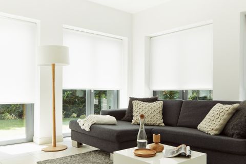 White hexham roller blind in large living room windows with grey sofa and wooden floor lamp