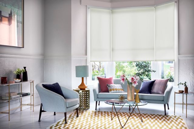 Grey living room with white bay-window blinds and warm, colourful furnishings