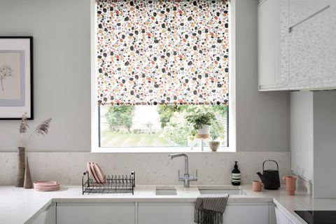 Marble kitchen with a white, blue, yellow, red and black patterned blind and warm accessories
